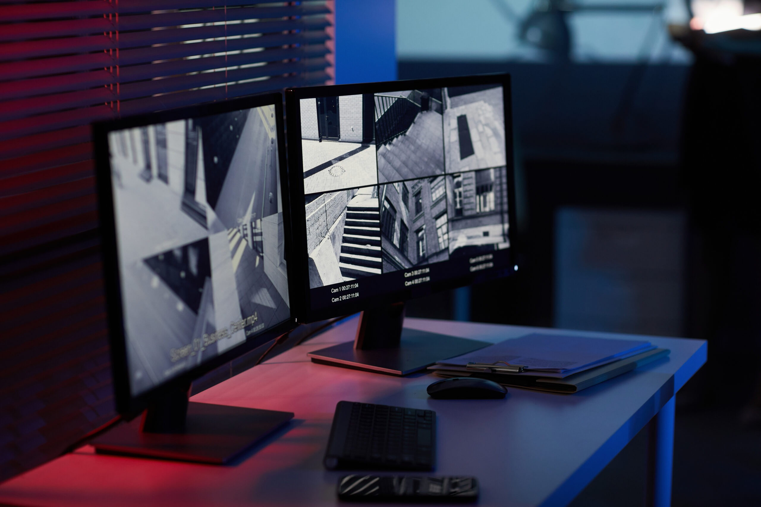 Background image of computer screens with surveillance camera footage in dark room with blue and red tones