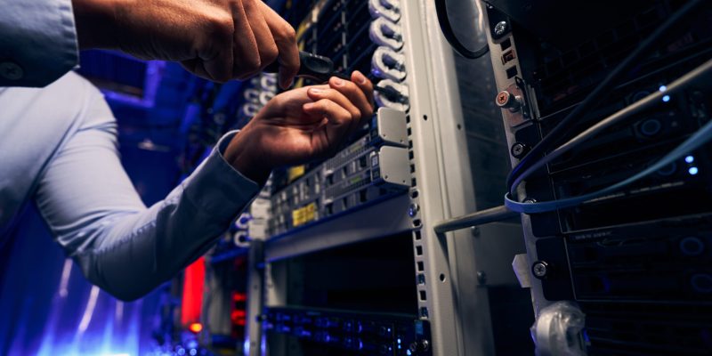 Cropped photo of data center engineer tightening screw on mounted hardware component using screwdriver